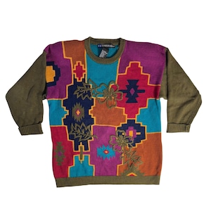 Może przedstawiać: Sweter w stylu vintage z patchworkowym wzorem w kolorze turkusowym, pomarańczowym, fioletowym i żółtym. Sweter posiada haftowane kwiatowe akcenty oraz oliwkowozielone rękawy i wykończenia. Etykieta głosi "ED DIFFUSION".