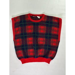 May include: A sleeveless sweater in a red, navy, and green plaid pattern. The sweater has a red ribbed neckline, armholes, and hem. The plaid design features large red squares with navy and green intersecting lines.