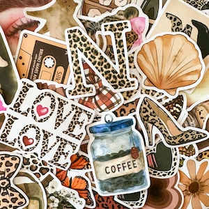 Puede incluir: Una colección de pegatinas con varios diseños. Incluye una concha, un zapato de tacón alto, la palabra "LOVE" con corazones y un tarro con la etiqueta "COFFEE". Otras pegatinas presentan estampado de leopardo y una cinta de cassette.