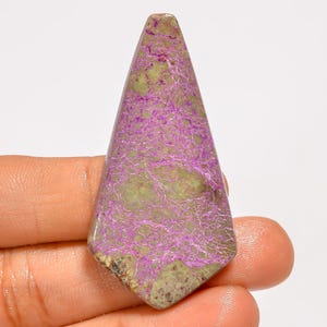 May include: A polished gemstone with a distinctive shape and colour. The stone has a light green base with intricate purple veining. The bottom edge has a speckled, darker appearance. A unique piece for jewellery.