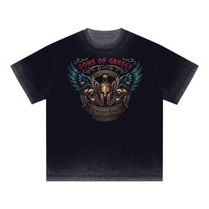 May include: Black t-shirt with a graphic design featuring the text "SONS OF GREECE" above a winged helmet and the text "Ανάγκα δ' οὐδὲ θεοὶ μάχονται" below. The design includes teal and gold accents.