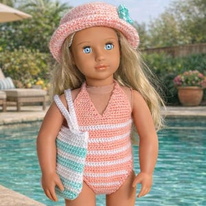 May include: A doll wearing a pink and white striped crochet swimsuit and matching hat with a turquoise bow. The doll is also carrying a white and turquoise striped crochet bag. The doll has blue eyes and blonde hair.