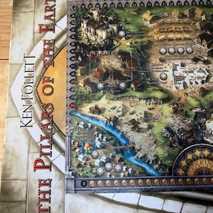 Puede incluir: Un juego de mesa titulado "The Pillars of the Earth" de Ken Follett. El tablero presenta un mapa detallado con ilustraciones de edificios, un río y un diseño similar a un reloj. El tablero está sobre una superficie de madera.