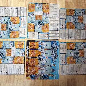 Op de afbeelding: Een verzameling bordspelcomponenten, waaronder kaarten en spelmatten. De matten zijn blauw en tonen de speltitel "Castle Combo" in een decoratief lettertype. De kaarten hebben verschillende illustraties en tekst, met een kleurenschema van geel, blauw en wit.