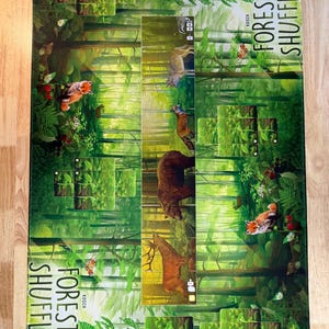 Pode incluir: Um jogo de tabuleiro intitulado "Forest Shuffle" com tema florestal. O tabuleiro apresenta ilustrações de vários animais da floresta, incluindo uma raposa, um urso e um veado, contra um fundo de árvores e folhagem. O título do jogo é exibido em texto branco.