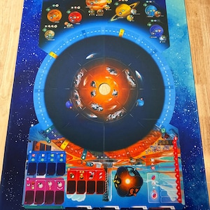 May include: A rectangular board game mat featuring a deep blue space background with a central circular track, illustrations of planets including Jupiter, Saturn, and Mars, and various game-specific icons, numerical scales, and card slots.