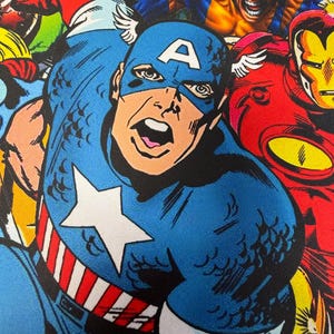 Può includere: Una vivace illustrazione a fumetti che ritrae Capitan America in una tuta blu con una stella bianca e strisce rosse e bianche. Accanto a lui, Wolverine in tuta gialla e blu e Iron Man in rosso e giallo, tutti rappresentati in azione.