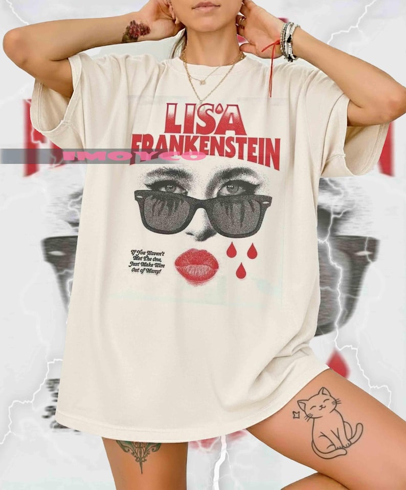 May include: Cream-colored t-shirt featuring the text "LISA FRANKENSTEIN" in red. The graphic includes a woman's face wearing sunglasses, red lips, and red teardrops. The shirt also has the text "If You Haven't Met The One, Just Make Mine Out of Many!"