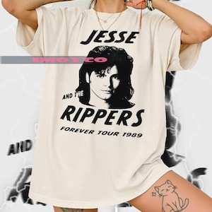 May include: Cream-colored t-shirt featuring a black and white graphic of a person and the text "JESSE AND THE RIPPERS FOREVER TOUR 1989". The shirt has a relaxed fit and short sleeves.