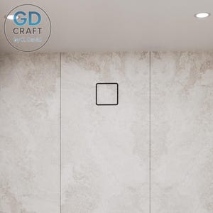 Op de afbeelding: Een close-up van een lichtgekleurde muur met een zwarte vierkante afvoerafdekking. De muur heeft een textuur die op marmer lijkt. De linkerbovenhoek heeft een cirkelvormig logo met de tekst "GD CRAFT by K. David".