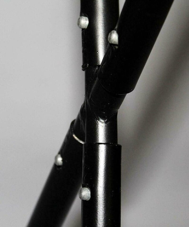 May include: Close-up of a black metal frame with intersecting curved bars. The frame has silver rivets at the joints. The glossy black finish reflects light, highlighting the curves and connections of the metal.