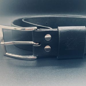 Peut inclure: Une ceinture en cuir noir avec une boucle argentée. La ceinture est ornée d'une boucle rectangulaire et fixée par des rivets argentés. La boucle de ceinture est également en cuir noir. Un accessoire classique.