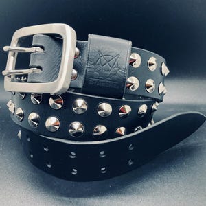 Könnte beinhalten: Schwarzer Ledergürtel mit silberfarbenen Metallnieten und einer großen quadratischen Schnalle. Der Gürtel hat ein geprägtes Design auf der Lederschlaufe. Ein Modeaccessoire für verschiedene Taillengrößen.