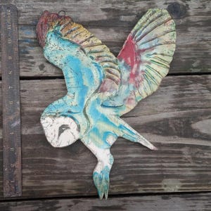 Peut inclure: Une décoration murale en forme de hibou, faite à la main. Le hibou présente un visage blanc, un corps bleu et des ailes avec des accents rouges, jaunes et verts. Les ailes sont déployées, et le hibou mesure environ 30 cm de long.