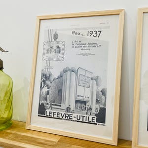 Peut inclure: Annonce publicitaire vintage encadrée pour les biscuits Lefevre-Utile, avec une illustration en noir et blanc d'un bâtiment et du texte. Le cadre est en bois clair. L'annonce comprend les années 1900...1937.