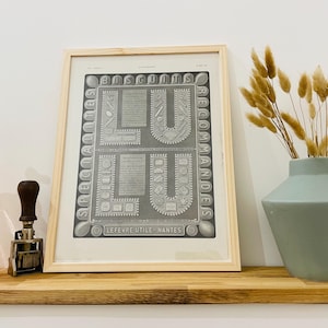 Peut inclure: Une publicité vintage encadrée pour les biscuits LU. L'impression en noir et blanc présente le mot "LU" dans une police décorative, entouré de texte et d'illustrations de biscuits. Le cadre est en bois clair.