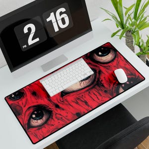 May include: A red and black desk mat with a detailed illustration of several eyes. A white keyboard and mouse are on the mat, with a computer monitor showing the time. The mat is rectangular and has a black border.