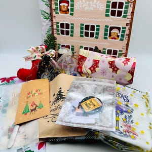 May include: A collection of Christmas-themed items including a gingerbread house advent calendar, a red stocking, a gift bag with a reindeer and Merry Christmas text, a clear pouch with a Books and Magic pin, and various patterned gift wraps.