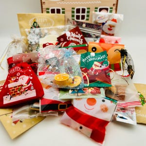 May include: A collection of assorted Christmas-themed gift bags and pouches featuring festive illustrations of Santa Claus, snowmen, and reindeer. The packaging includes red velvet drawstring bags, clear organza pouches, and printed paper envelopes with Merry Christmas text.