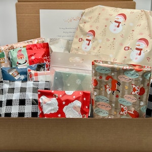 May include: A cardboard box filled with wrapped gifts. The gifts are wrapped in various festive papers, including snowmen, foxes, and Santa Claus designs. A card with text is visible. The box is open, revealing the contents.