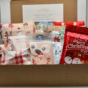 May include: A cardboard box filled with wrapped gifts and a greeting card. The gifts are wrapped in various festive papers with holiday designs, including snowmen, reindeer, and plaid patterns. A red bag with "Merry Christmas" text is visible.