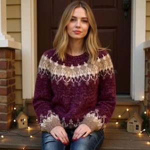 Op de afbeelding: Een bordeauxrode trui met een ronde hals en een patroon in beige en wit. De trui heeft lange mouwen en is gemaakt van een zacht, getextureerd materiaal. Het model draagt een blauwe spijkerbroek.