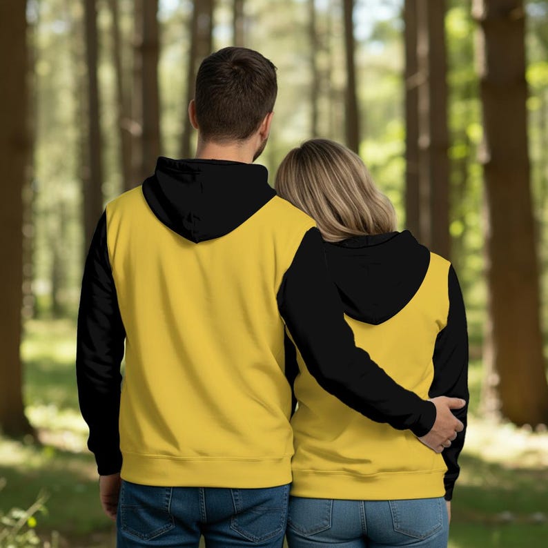 K&ouml;nnte beinhalten: Zwei Personen tragen passende Kapuzenpullover. Die Kapuzenpullover haben schwarze &Auml;rmel und Kapuzen sowie einen gelben K&ouml;rper. Das Paar steht in einem Wald, von hinten gesehen. Die Kapuzenpullover sind wahrscheinlich aus weichem Material.