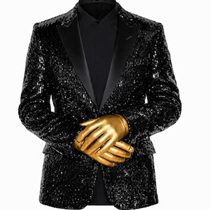 May include: A black sequined blazer featuring a solid black lapel and a black button-down shirt underneath. The garment is displayed with a pair of metallic gold gloves positioned at the center, showcasing a reflective surface and detailed stitching.