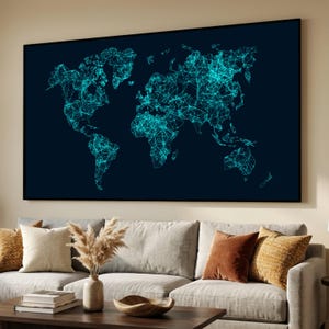 May include: A large, framed wall art piece featuring a world map design. The map is rendered in a network style with interconnected lines and nodes, using a vibrant teal color against a dark navy blue background. The artwork is displayed above a gray sofa.