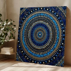 May include: A square canvas print displaying a detailed mandala design in blue and gold. The artwork features concentric circles with intricate dot patterns and textures, creating a visually captivating piece. The colour palette includes deep blues, teal, and gold accents.