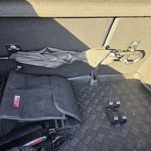 May include: A car trunk interior with a black umbrella, a dark gray mat, and various accessories. The trunk has a black rubber floor mat with a diamond pattern. The umbrella is secured in a holder.