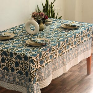Puede incluir: Un mantel rectangular con un estampado floral azul y un borde blanco. La mesa está puesta con platos, servilletas y un jarrón. El mantel está hecho de una tela suave y duradera.