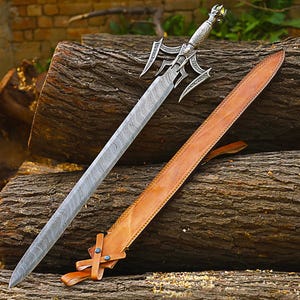 May include: A silver sword with an ornate handle and a brown leather sheath rests on a pile of logs. The sword has a patterned blade and a decorative hilt. The sheath is tan and has a strap.