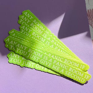 May include: A stack of bright green stickers with a wavy edge. Each sticker has the text "ANY ROOM IS A PANIC ROOM IF YOU JUST GIVE ME A SECOND" in white. The stickers are on a purple surface.