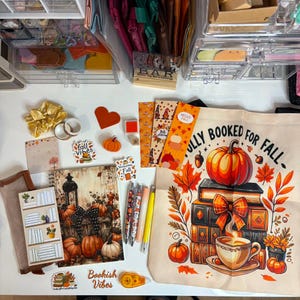 May include: A collection of autumn-themed stationery and accessories including a canvas tote bag with the text FULLY BOOKED FOR FALL, a spiral notebook with a pumpkin and lantern illustration, bookmarks, pens, stickers, a scrunchie, and a notepad.