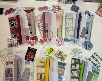 May include: A collection of book trackers, stickers, and pens. The trackers feature bookshelf designs and text like "Book Lover" and "Read More Books." Pens are in various colors, including pink, yellow, and green. Stickers have phrases like "Good Vibes Only."