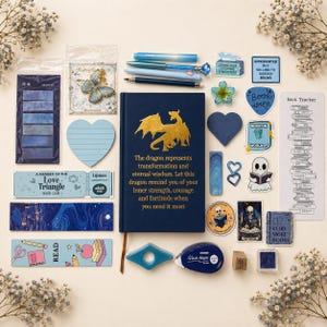Peut inclure: Divers articles de papeterie et sur le thème des livres, dont un journal bleu marine avec un motif de dragon doré, des autocollants, des stylos et des marque-pages. Les articles sont disposés sur un fond clair avec des accents floraux.