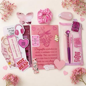 Peut inclure: Ensemble de papeterie et d'accessoires roses, comprenant un carnet, des stylos, des autocollants, un chouchou et une décoration en forme de papillon. Le carnet présente un motif de libellule et du texte. Le thème est centré sur les livres et la lecture.
