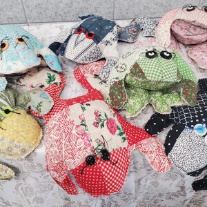 Puede incluir: Una colección de siete peluches de rana de tela hechos a mano con diversos textiles estampados, incluyendo motivos florales, de cuadros vichy y de lunares. Cada animal de peluche presenta ojos de botón y detalles cosidos.