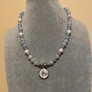 May include: A beaded necklace featuring gray and white stones, interspersed with silver-colored beads. The necklace has a pendant with the Japanese character for "harmony" or "peace" on a white background.