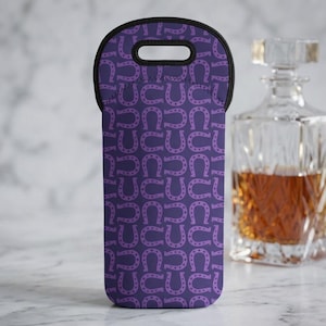 Peut inclure: Sac de bouteille de vin violet avec un motif de fer à cheval répété. Le sac a une poignée noire et est fait d'un matériau semblable au néoprène. Une carafe en verre transparent avec du liquide ambré est en arrière-plan.