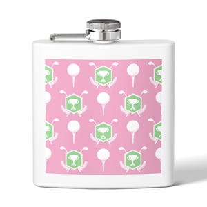 May include: White flask with a silver cap and hinge. The front features a pink background with a repeating pattern of white golf balls on tees, green golf club and trophy emblems.