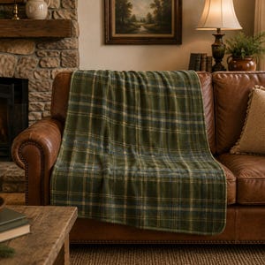 Peut inclure: Un plaid rectangulaire orné d'un motif à carreaux classique dans des tons de vert forêt, bleu marine et de fines rayures crème. Le tissu présente un aspect doux et texturé, drapé sur l'assise d'un canapé en cuir marron.