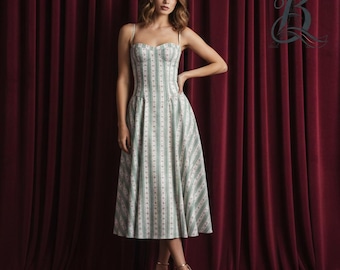 Könnte beinhalten: Ein hellgrünes und weiß gestreiftes Midikleid mit herzförmigem Ausschnitt und Spaghettiträgern. Das Kleid hat ein figurbetontes Oberteil und einen ausgestellten Rock. Das Model trägt goldene Absätze. Der Hintergrund ist ein dunkelroter Vorhang.