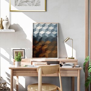 May include: A wooden desk with a framed geometric art print featuring a cube pattern in shades of blue and brown. A small desk lamp, a potted plant, and a chair are also visible.