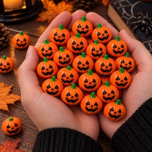 Può includere: Una collezione di piccole perline a forma di zucca in plastica arancione brillante, ognuna con un volto di jack-o'-lantern intagliato con occhi, naso triangolare e bocca frastagliata dipinti di nero. Le zucche hanno un piccolo stelo verde in cima.