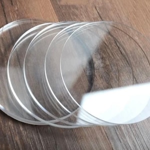 Könnte beinhalten: Ein Set aus fünf kreisförmigen, transparenten Acrylscheiben, die leicht überlappend in einer fächerartigen Formation angeordnet sind. Jede Scheibe hat eine glatte, klare Oberfläche mit polierten Kanten, was ein einheitliches Erscheinungsbild ergibt.