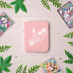 Pu&ograve; includere: Un raccoglitore per carte rettangolare rosa chiaro con un'illustrazione a linee bianche del personaggio Eevee circondato da piccoli fiori di ciliegio. Il raccoglitore ha angoli arrotondati e una finitura esterna liscia e tinta unita.