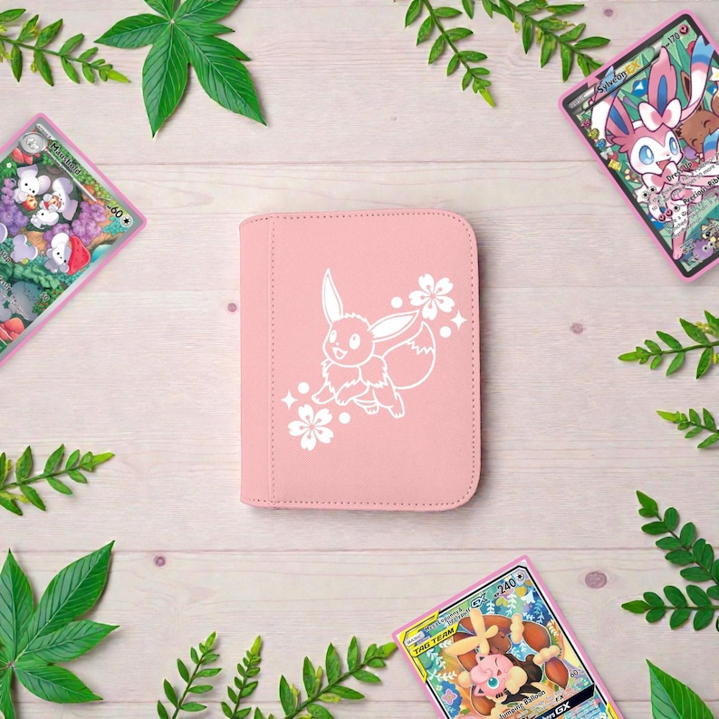 Pu&ograve; includere: Un raccoglitore per carte rettangolare rosa chiaro con un'illustrazione a linee bianche del personaggio Eevee circondato da piccoli fiori di ciliegio. Il raccoglitore ha angoli arrotondati e una finitura esterna liscia e tinta unita.