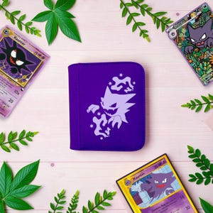 Pu&ograve; includere: Un raccoglitore per carte viola con una sagoma bianca della creatura di tipo spettro Haunter circondata da piccole forme a stella. Il raccoglitore &egrave; posizionato tra tre carte collezionabili che raffigurano la stessa creatura e rametti verdi.